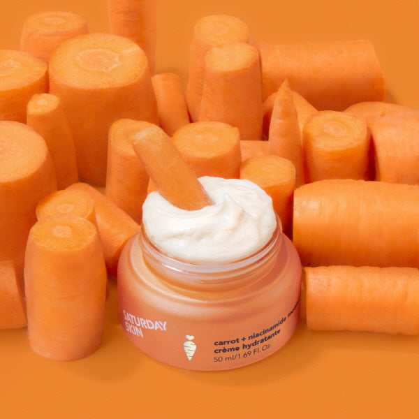 Jar of cream surrounded by carrots on an orange background