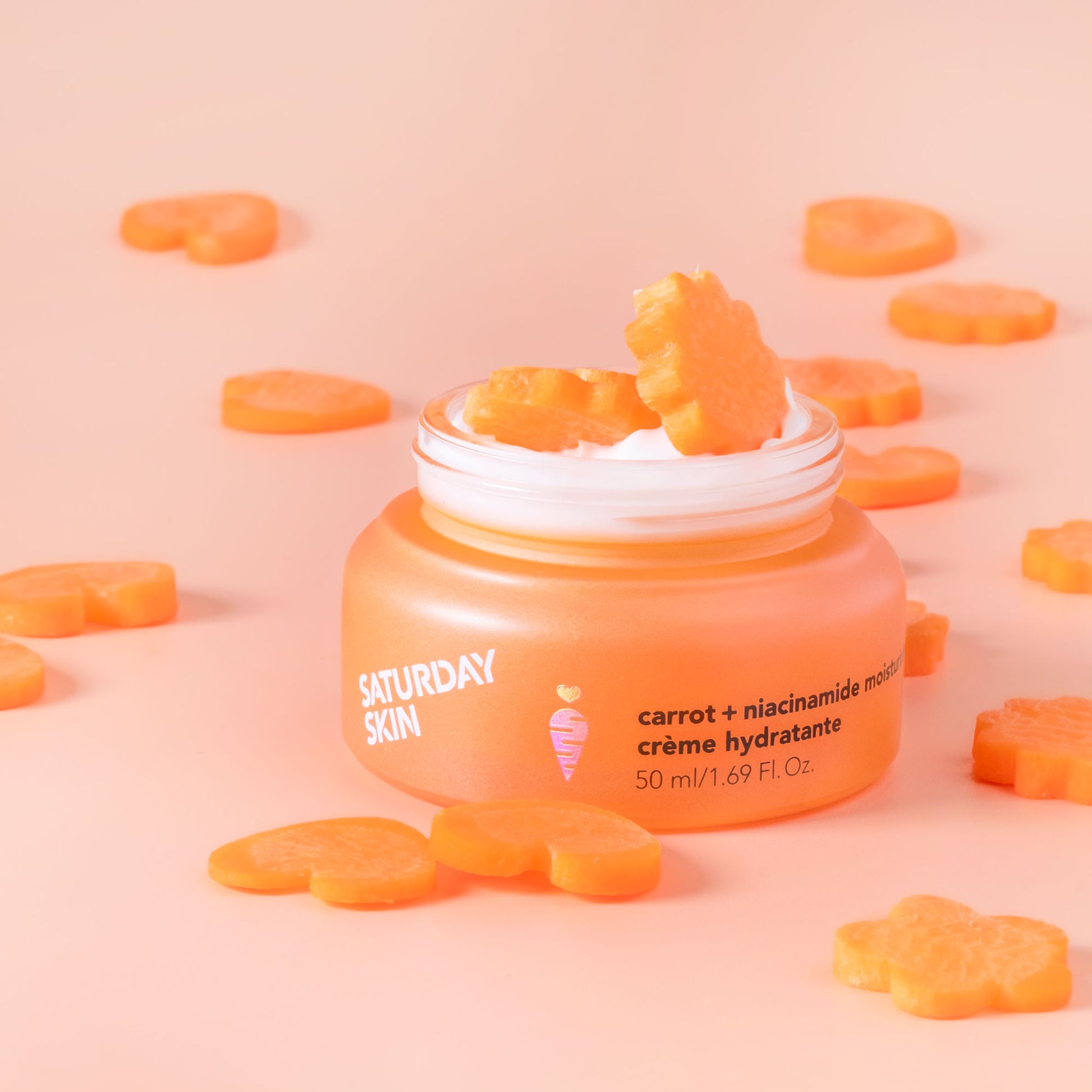 Jar of 'Saturday Skin' cream with carrot-shaped candies on a pink background