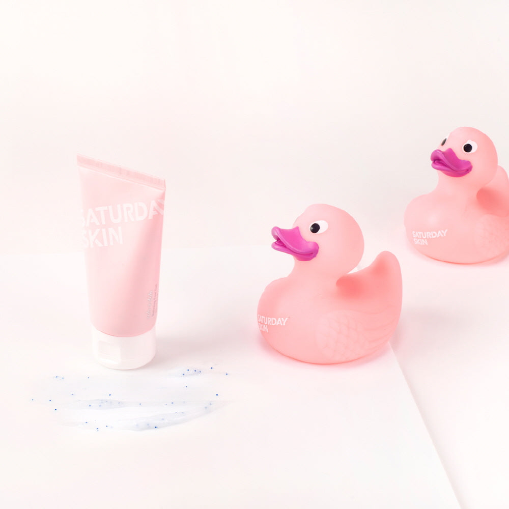 Two pink rubber ducks and a pink tube of cream on a white background