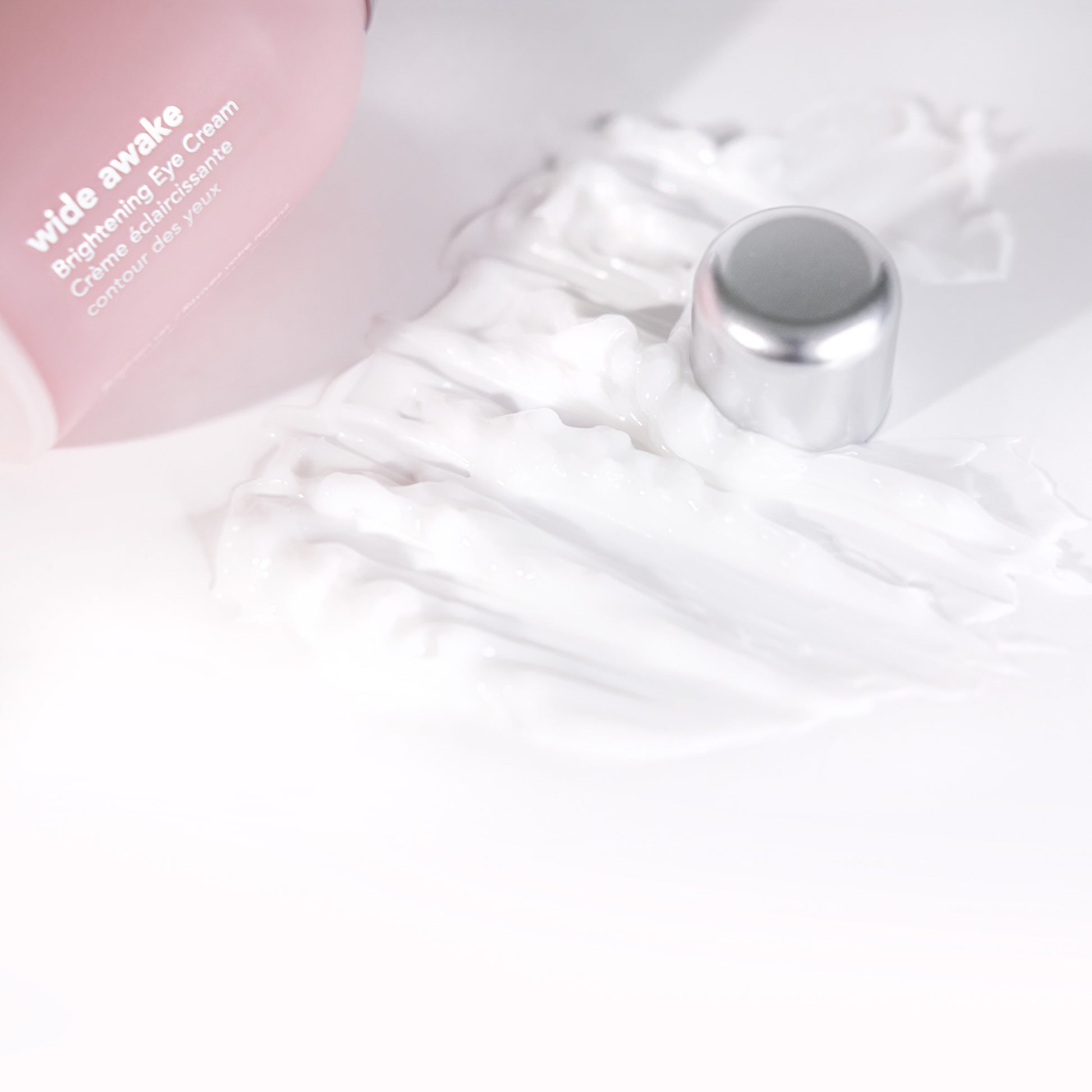 Pink eye cream bottle with a silver cap on a white marble surface