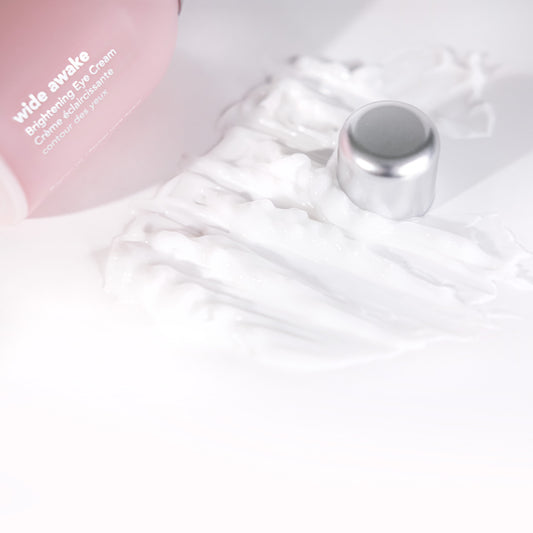 Pink eye cream bottle with a silver cap on a white marble surface